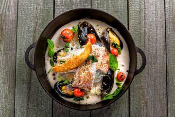 Bowl of delicious seafood meal with rice noodles. Meal made of sea bass fish, mussels, crab meat and other seafood with vegetables on a table. Top view.