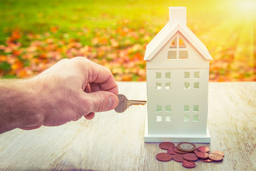 Home insurance concept. Safety of family and home. key in hand closes miniature house with money coins. Save property in house on background of sunny green grass.