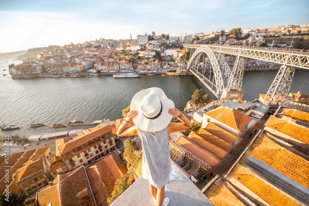 Young woman tourist enjoying beautiful landscape view on the old town with river and famous iron bridge during the sunset in Porto city, Portugal - obrazy, fototapety, plakaty 