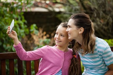 Wall Mural - Smiling daughter taking selfie with mother sitting on bench