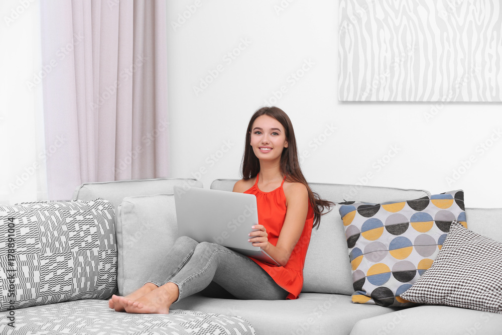Young lady with modern laptop sitting on sofa at home