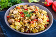 Light healthy dietary salad with couscous, vegetables (zucchini, eggplant, carrots, sweet peppers, onions), chicken pieces on a dark wooden background.