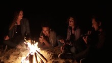 Round Camera Movement: Multiracial Group Of Young Boys And Girls Sitting By The Bonfire Late At Night And Singing Songs And Playing Guitar. Cheerful African American Playing Guitar By The Fire