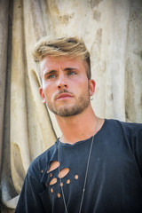 Wall Mural - Handsome blond, blue eyed young man leaning against stone wall outdoor and looking to a side in Turin, Italy