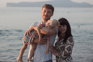 Mom, Dad and daughter. Dad holds a daughter in her arms. Everyone looks at the camera. Sea. Happiness. Dawn.