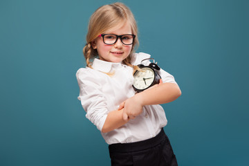 Wall Mural - Adorable cute little girl in white shirt, glasses and black trousers hold alarm clock