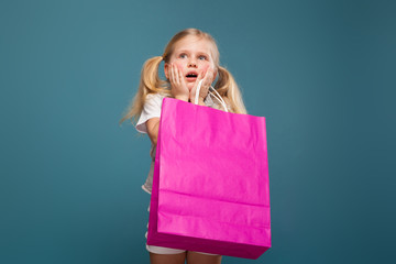 Wall Mural - Adorable cute little girl in white shirt, white jacket and white trousers hold purple paper bag