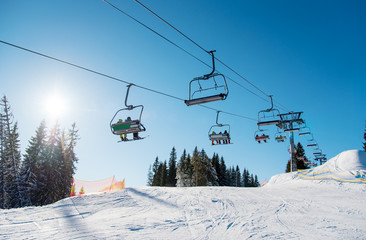 Low angle shot of a ski lift at ski resort Bukovel in the mountains on a sunny winter day. Blue sky, sun and forest on the background copyspace riding top nature extreme sport recreation concept