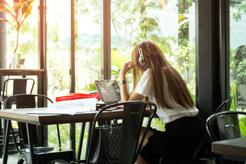 Asian students in uniform with headphone studying in coffee shop using laptop