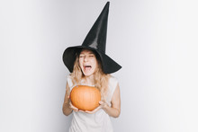 A Young Girl In A White Shirt And A Black Hat With Pumpkin In Hands Crying In Fear, Closing Eyes, On A White Background