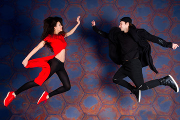 Couple of hip hop / R&B / break dancers jumping to each other wearing in stylish modern red and black cloth on industrial background with rusty hexagonal cells