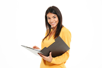 Wall Mural - Smiling brunette woman in yellow shirt holding clipboard, looking at camera