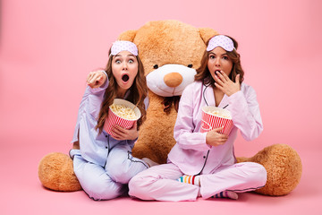  Two scared pretty girls dressed in pajamas pointing finger