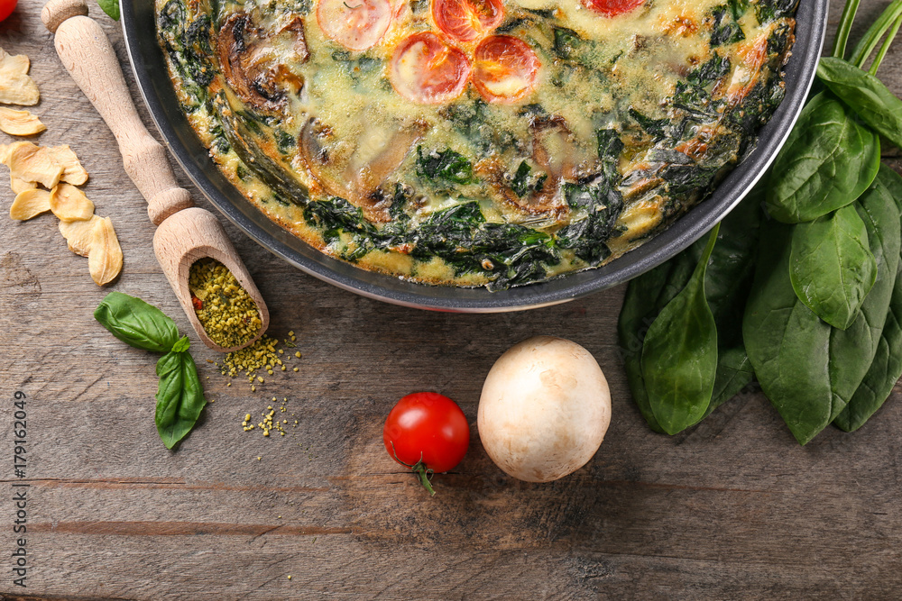 Frying pan with delicious spinach frittata on wooden background