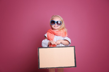 Little girl playing with cardboard suitcase on color background