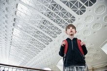 Boy With Backpack Stands In A Station, Waiting For His Train