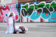 Several used spray cans with pink and white paint and caps for spraying paint under pressure is lies on the asphalt near the painted wall in colored graffiti drawings