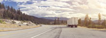 A Panorama Of Beautiful Mountainous Landscape With A Highway Running Through It And A 18-wheeler Stopped On The Shoulder