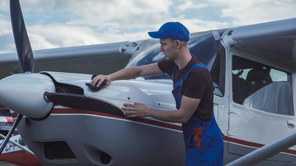 Young pilot or mechanic working on an aircraft wiping down the nose cowling on a small plane parked outdoors on an airfield