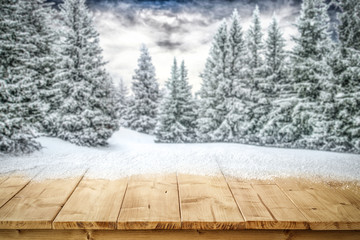 A table full of snowflakes with space for your product advertisement. Winter landscape of trees covered with snow and overcast with blue dramatic sky.