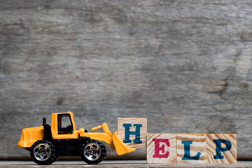 Sticker - Yellow plastic bulldozer hold letter H to complete word help on wood background