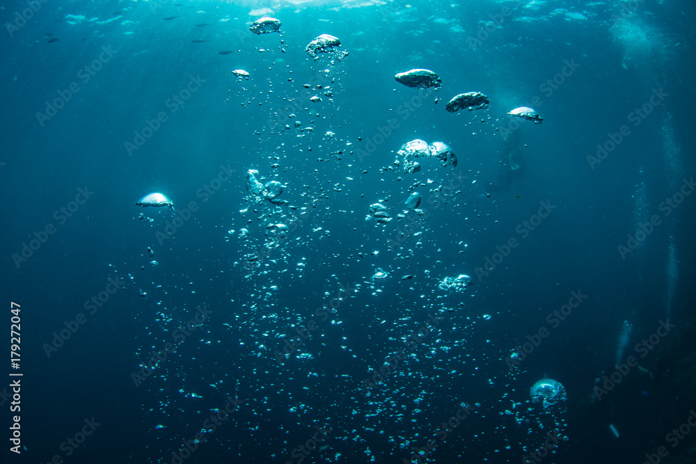 Underwater shot of blue ocean water, air bubbles closeup, sunbeams on water surface, some scubadivers in deep - obrazy, fototapety, plakaty 