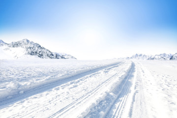 Sticker - Winter Background of foreground of road covered with snow and ice. In the background, the arctic landscape of the mountains with the beautiful blue sky.