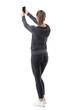 © sharplaninac - Rear view of sporty athletic woman taking selfie while holding cellphone in both hands. Full body length portrait isolated on white background.