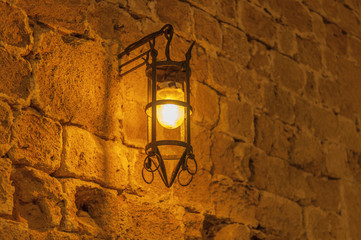 Close old light at night hanging on a medieval street fortress wall