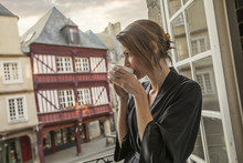 Caucasian Woman Drinking Coffee On Balcony In City