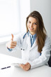 © zadorozhna - Smiling doctor showing thumb up while sitting in office