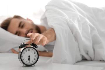 Wall Mural - Young man switching off alarm clock signal while lying in bed at home