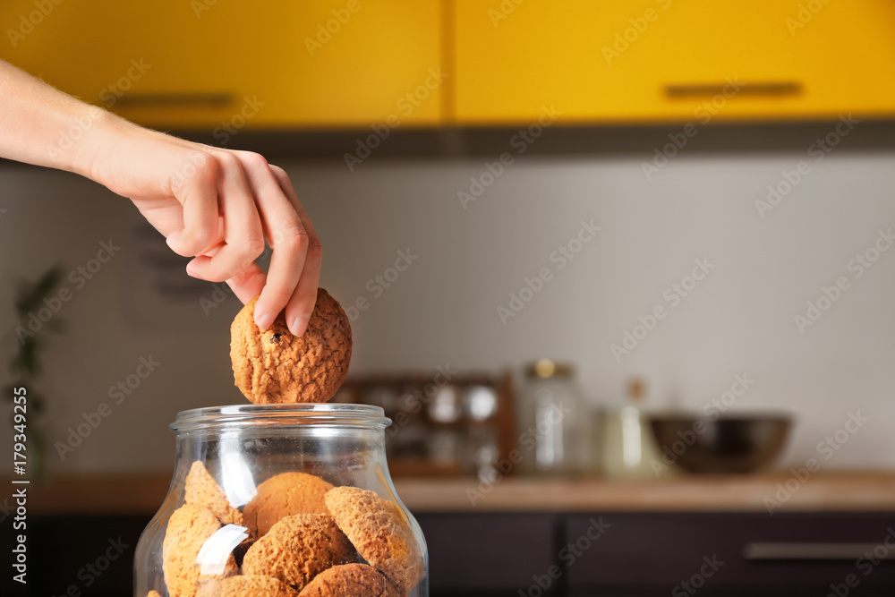 Woman taking oatmeal cookie from glass jar