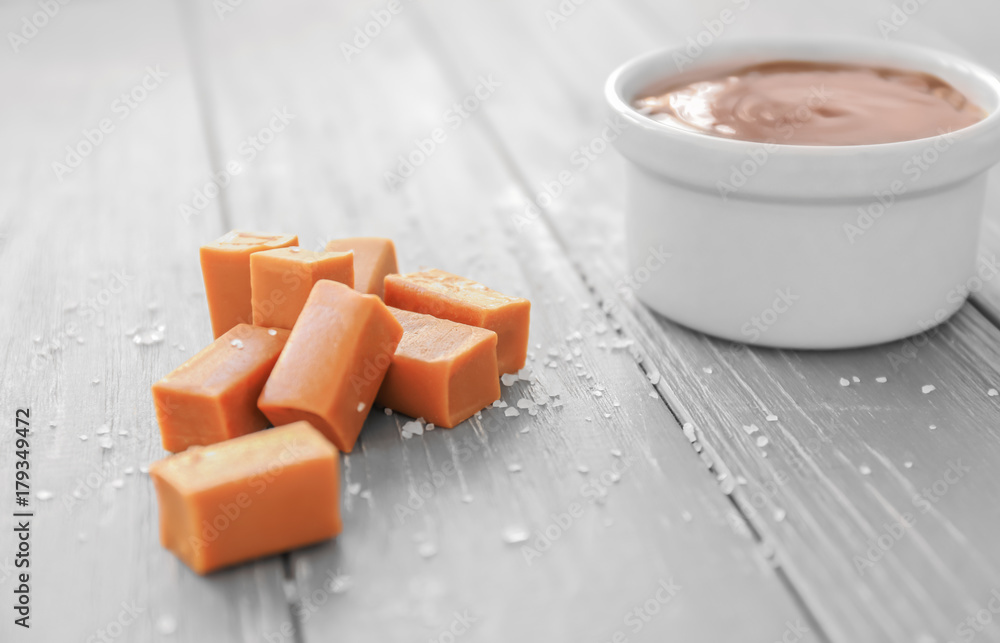 Candies and bowl with caramel topping on wooden table