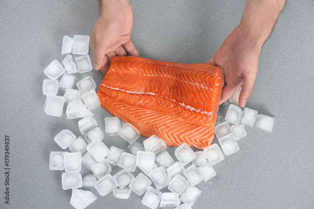 Man putting fresh salmon fillet on table in kitchen