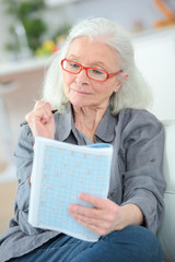 pensioner wearing reading glasses doing magazine puzzle