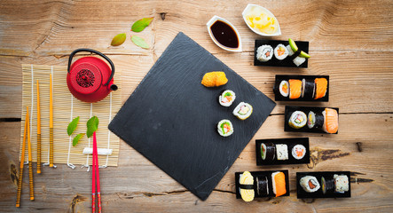 Wall Mural - Red teapot, green leaves, slate tray and red chopsticks on old wooden table, asian background, top view, healthy wood and diet concept