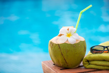 Coconut With A Straw On The Edge Of A Deckchair Against A Blue Water Pool Background