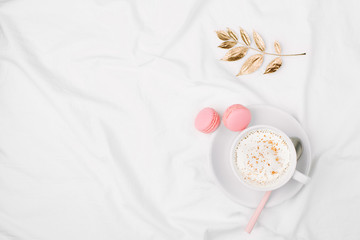 Cup of coffee and macaroons on bed with golden autumn leaf. Copy space. Flat lay, top view