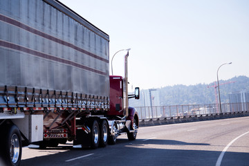 Red big rig day cab semi truck with covered trailer turning on overpass city road