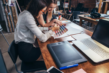 Wall Mural - two female architects working together using color swatches sitting at desk with laptop, graphic tab