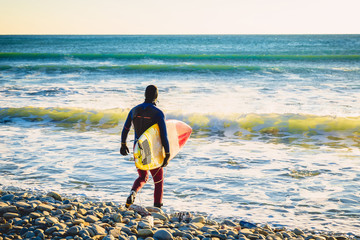 Surfer with surfboard on beach at sunset or sunrise. Surfer and ocean waves