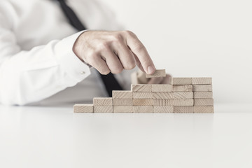 Wall Mural - Front closeup view of businessman constructing steps of wooden pegs