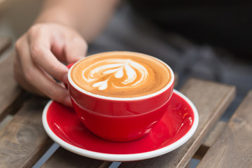 Women hand holding a cup of latte coffee with latte art in the cafe.