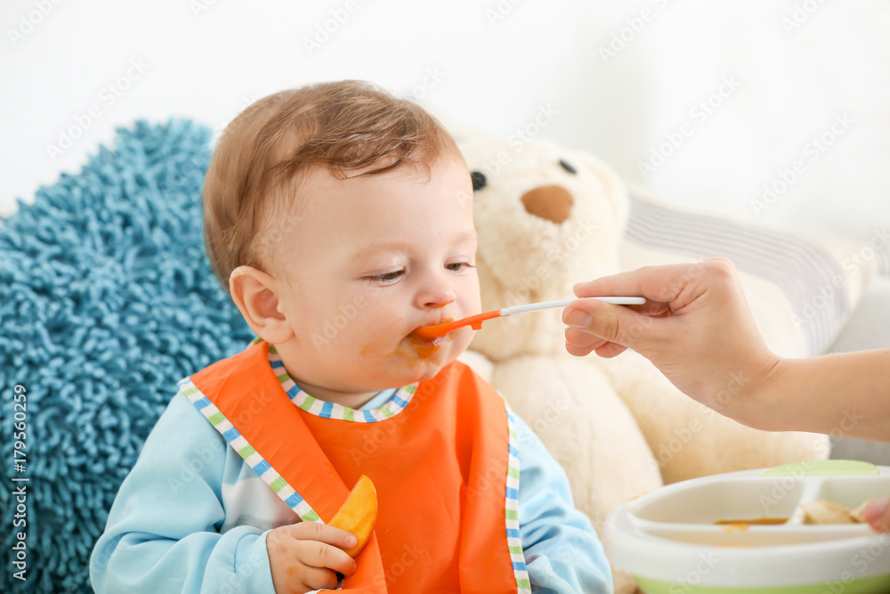 Mother feeding baby with spoon indoors