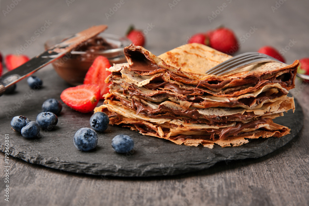 Slate plate with thin pancakes, chocolate paste and berries on table