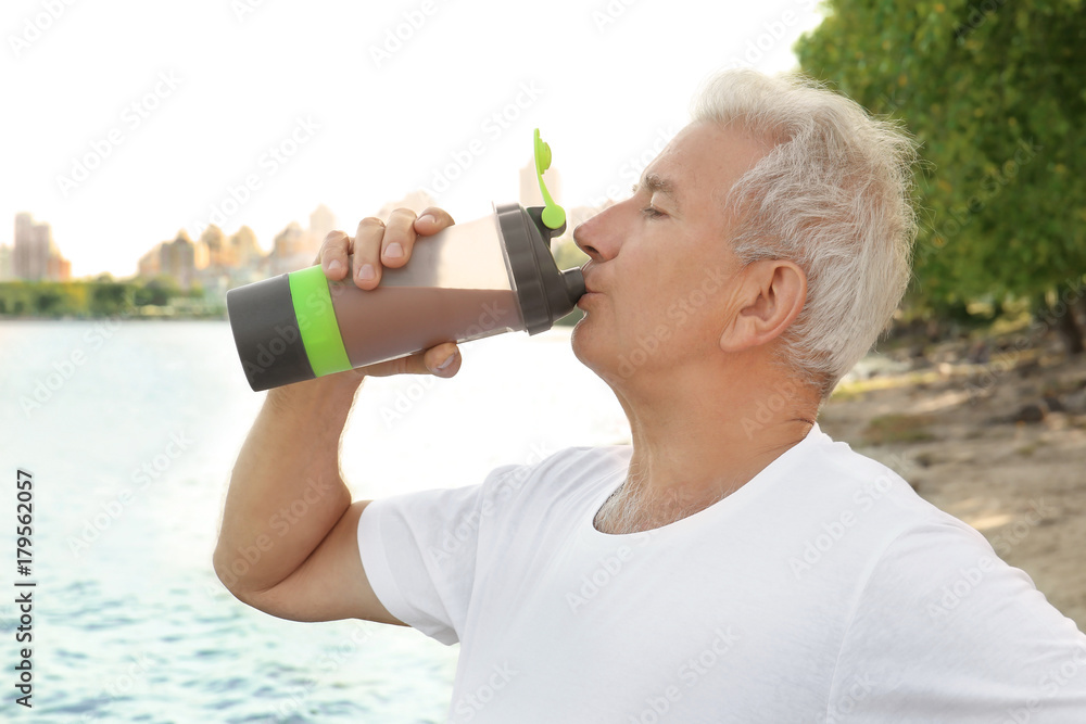 Sporty senior man drinking protein shake, outdoors