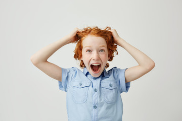 Close up of funny little boy with red hair and freckles pulling hair with hands,screaming with surprised expression, being super happy new gyroscooter for birthday.