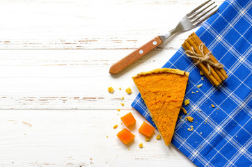 Pumpkin  pie, cinnamon sticks, autumn dry leaves on white wooden table