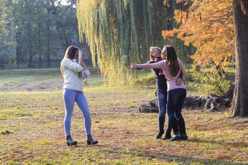 Three girls havin fun in park, one of them have old film camera and taking pictures of two young long hair girls who posing